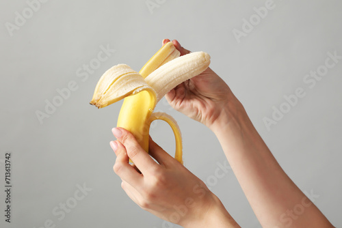 Young woman peeling banana on light background, closeup. Sex concept