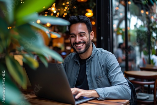 Smiling young Latin business man using laptop sitting outdoor. Happy guy student or professional looking away in city cafe elearning, hybrid working, searching job online thinking of digital solution