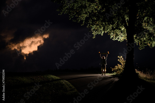 Silhouette of a young girl with a longboard, which she holds above her head with two hands against the background of a beautiful night sky