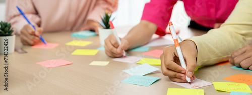 Group of young business group brainstorms ideas on colorful sticky notes. A portrait of startup group planing marketing strategy while writing down on sticky note at office meeting room. Variegated.