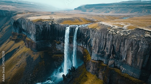 an aerial view of a waterfall in the middle of a rocky area with yellow grass on the ground and brown grass on the ground, and yellow grass on the ground.