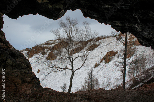 View from through cave on snowy mount with rocks and tree. Rock formation Natural arch creates a frame, siberian winter landscape. Torgashinsky ridge Krasnoyarsk, Siberia, Russia. Famous travel place
