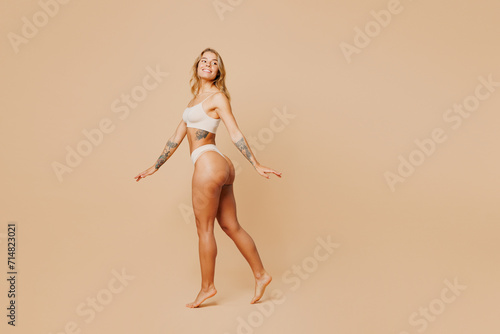 Full body side view young nice lady woman with slim body perfect skin wear nude top bra lingerie stand walk go look aside on area isolated on plain pastel beige background. Lifestyle diet fit concept.
