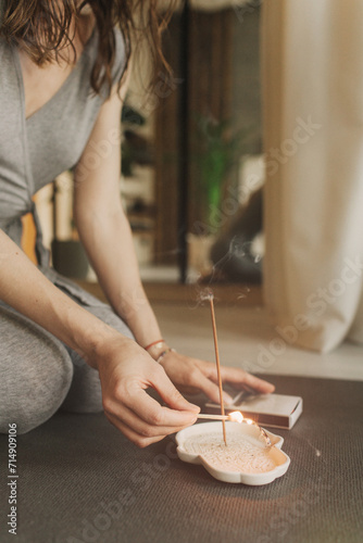 A young woman lighting incense sticks an home before yoga. Buddhist healing practices. Clearing the space of negative energy. Aromatherapy. Selective focus
