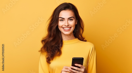 Beautiful young brunette woman holding a phone on yellow background