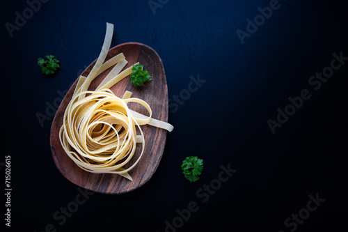 Dried pasta fettuccine or tagliatelle, linguini on wooden plate.