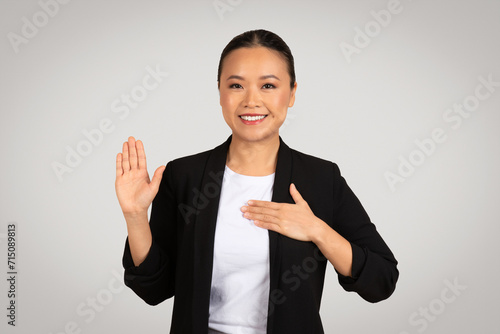 Professional Asian businesswoman making a pledge or oath gesture with a raised right hand
