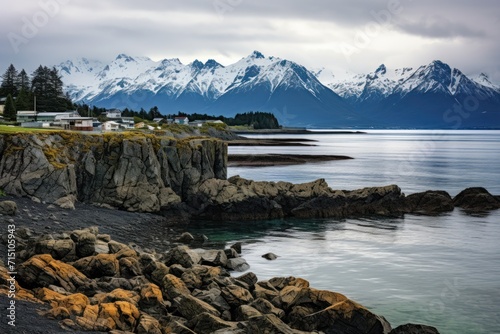  a body of water surrounded by a rocky shore with a mountain range in the background and houses in the foreground.