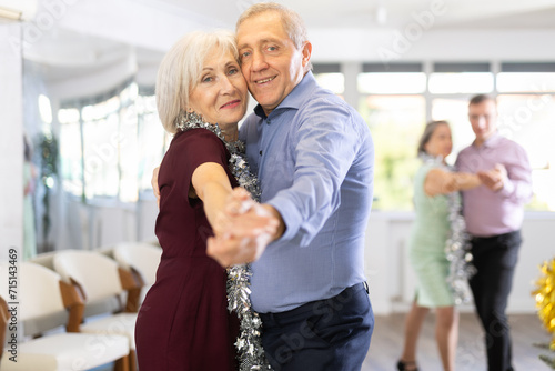 Against background of Christmas tree and decorations in studio, elderly couple enthusiastically dances rock and roll. Pleasant pastime and active hobby