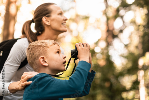Mother child together hiking in the forest looking through binoculars bird watching exploring learning about nature, family adventure 