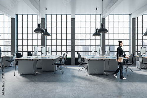 Pretty blurry woman walking in modern coworking office interior with large panoramic windows with city view, lamps, concrete flooring and other objects.