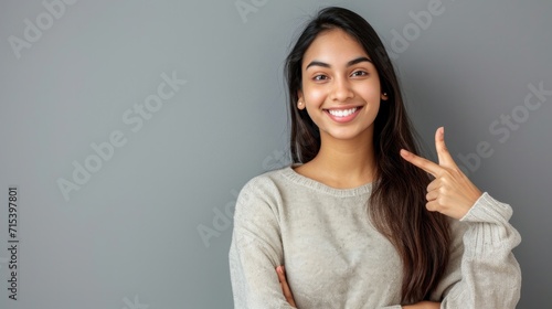 Young Indian woman pointing at gray background with blank space on her hand Happy female student looking at camera advertising product service concept sign