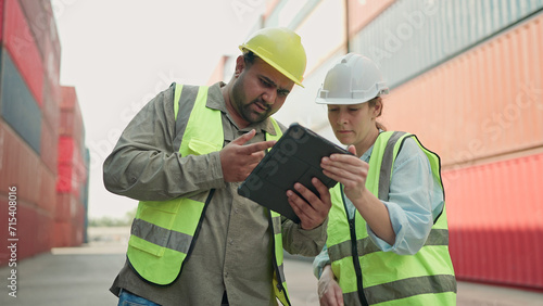 Two industrial workers in hardhats using tablet working together in container yard. Cargo shipping import and export industry. Logistic shipping yard business. Teamwork concept