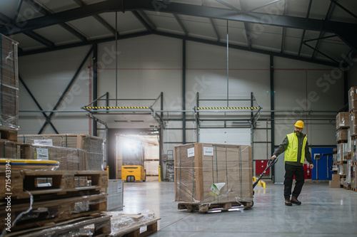 Warehouse worker maneuvering pallet jack loaded with goods through warehouse.