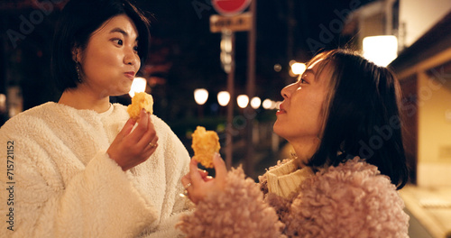 Woman, friends and street food or eating Japanese snack for travel experience, hungry or local trip. Female people, sidewalk and night walk on vacation for nutrition culture, adventure or traditional