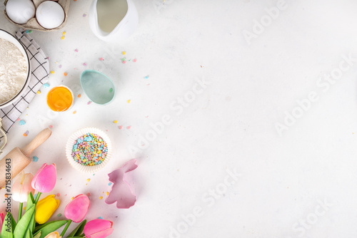 Easter baking background, ingredient for making Easter cookies, cakes, dessert with Easter chocolate eggs, sugar sprinkles, baking ingredients, flour, egg, milk, rolling pin, spring flowers top view