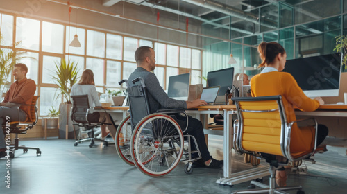 personne handicapée en fauteuil roulant travaillant sur son ordinateur dans un open space avec d'autres personnes valides 