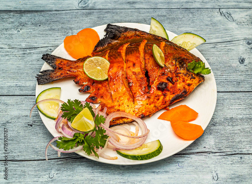 tandoori pomfret fish fry with lemon and onion served in dish isolated on wooden table top view of indian spicy food