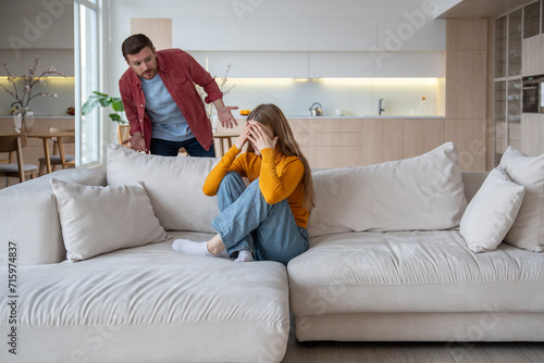 Annoyed offended woman sitting on sofa, closing face with hands, thinking of marital discord, conflict, problems in relations. Bewildered man justifying, expaining behaviour, mistake. Toxic relations