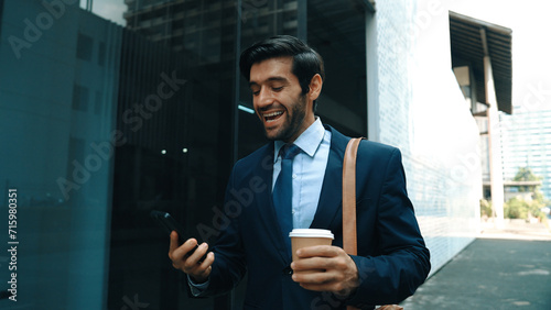 Smart manager looking at mobile phone and walking at street while wearing suit. Skilled investor looking mobile phone to checking sales or working while holding coffee cup. White background. Exultant.