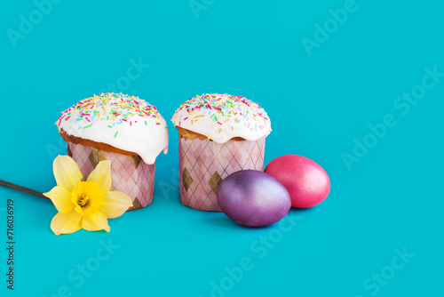 Traditional russian Easter ortodox cake with daffodil flower and colorful eggs on light pink background. Kulic, Kulich, Paska homemade bread with glaze. Spring christian holiday. Festive celebration