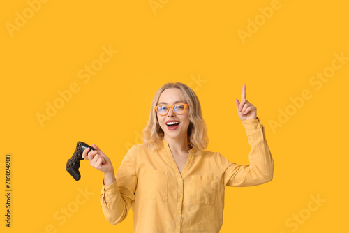Pretty young woman with game pad pointing at something on yellow background