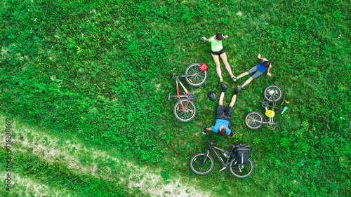 Family cycling on bikes aerial drone view from above, happy active parents with child have fun and relax on grass with bicycles, family sport and fitness outdoors 