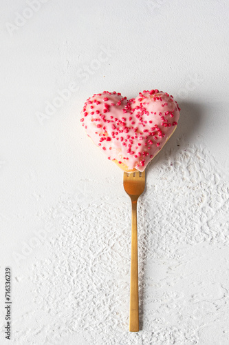 A heart-shaped doughnut with pink icing and red sprinkles on a golden fork, Happy valentine day greeting card