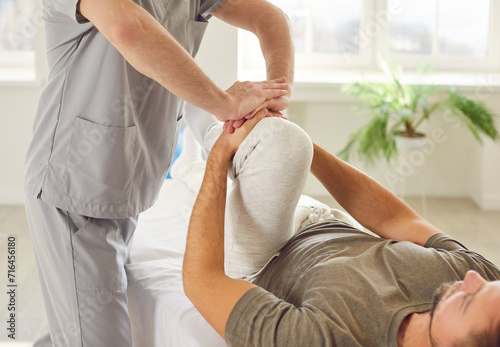 Male physical therapist doing healing treatment on mans knee in rehabilitation clinic. Professional physiotherapist or osteopath working in office. Physiotherapy and osteopathic medicine concept.