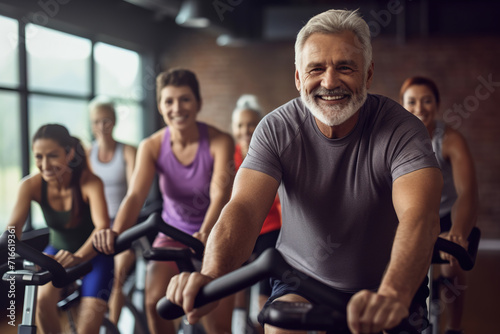 Fit mature man in sportswear doing a cycling class in a gym with a diverse group of people.