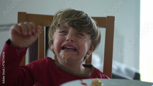 Small boy having a tantrum at lunch table. close-up face of child hitting table and crying displeased and with messy mouth