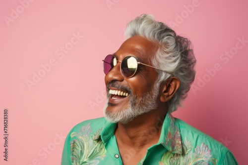 Portrait of a joyful indian man in his 60s wearing a trendy sunglasses against a pastel or soft colors background. AI Generation