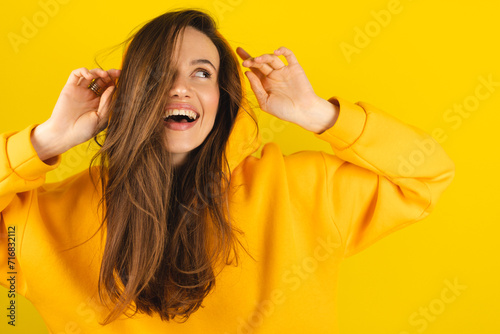 Close up photo of trendy cheerful cute nice sweet youngster laughing looking away toothy wearing hood isolated over yellow color background. Funny girl look playful holding hood.