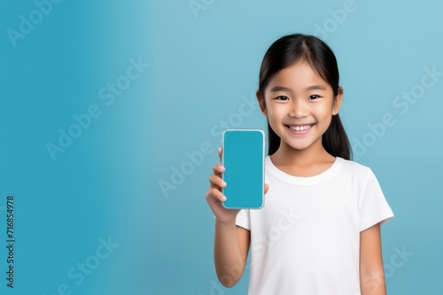 Happy kid tween teen asian girl holding phone smartphone mock up showing white blank display for advertising