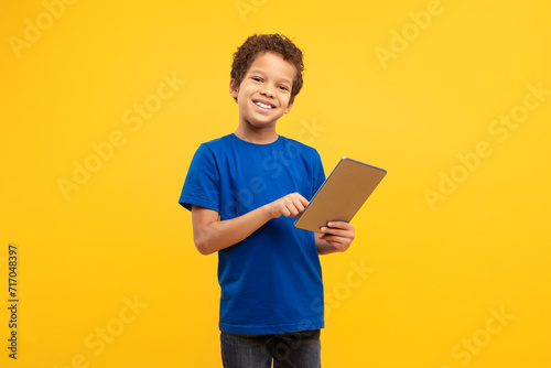 Smiling boy using digital tablet in blue shirt, yellow background