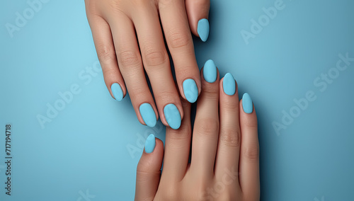 manos tocándose con las uñas pintadas en azul pastel, posadas sobre superficie de mismo color