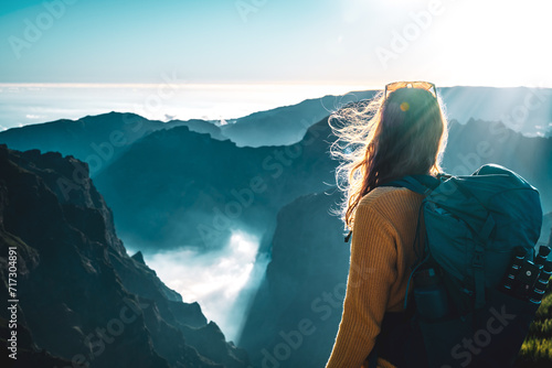 Female backpacker tourist looking at a deep, cloud-covered valley and enjoying the breathtaking view of the volcanic mountain landscape. Pico do Arieiro, Madeira Island, Portugal, Europe.