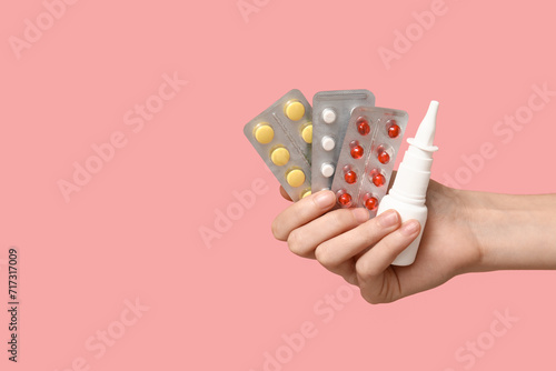 Female hand holding pills in blister packs and nasal spray on pink background