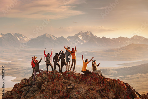 Big group of happy tourists are having fun and greeting sunset at mountain top. Active vacations concept