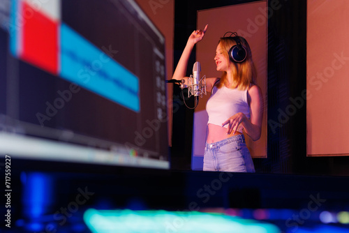 Young professional female singer with headphones performs a song with a microphone while recording in a music studio