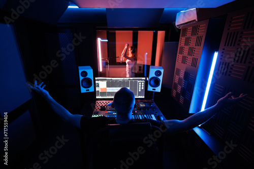 The sound engineer makes a recording in the studio and adjusts the sound parameters. A young female singer is recording a song