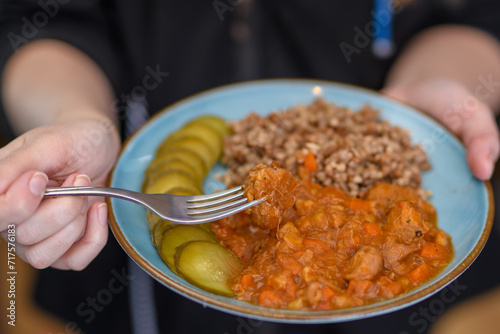 Jeść na stojąco, kobieta trzyma talerz z obiadem z kasza gryczana i mięsem duszonym w sosie własnym