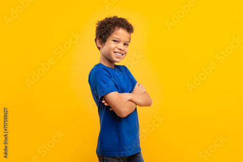 Confident boy with arms crossed in blue shirt on yellow background