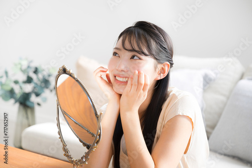 鏡をみて肌のチェックするアジア系（日本人）笑顔の女性 スキンケアのイメージ 見上げる