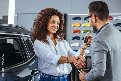 Smiling woman receiving her car keys in auto saloon. Happy salesman congratulating his female customer for buying a new car