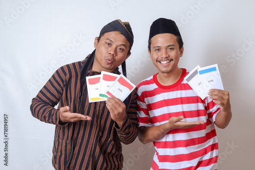 Portrait of two excited Indonesian man from Javanese and Madurese tribes holding voting paper for General Election (Pemilu) of president and government of Indonesia. Isolated image on gray background