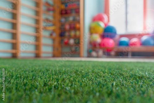 Sport class room with artificial carpet with green grass is filled with sports equipment toys and fitness balls for children physical education or medical rehabilitation