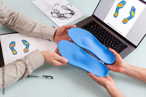 Female doctor orthopedist presents new custom made insoles to a male patient in a clinic.