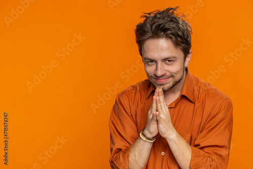 Sneaky cunning Caucasian young man with tricky face gesticulating and scheming evil plan, thinking over devious villain idea, cheats, jokes pranks. Guy isolated on orange studio background. Copy-space
