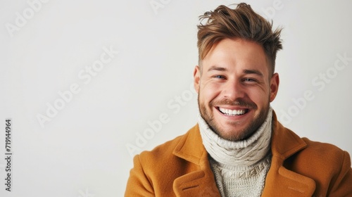 Young handsome kind man with beard wearing casual sweater and brown yellows coat over white background happy face smiling looking at the camera. Positive person.